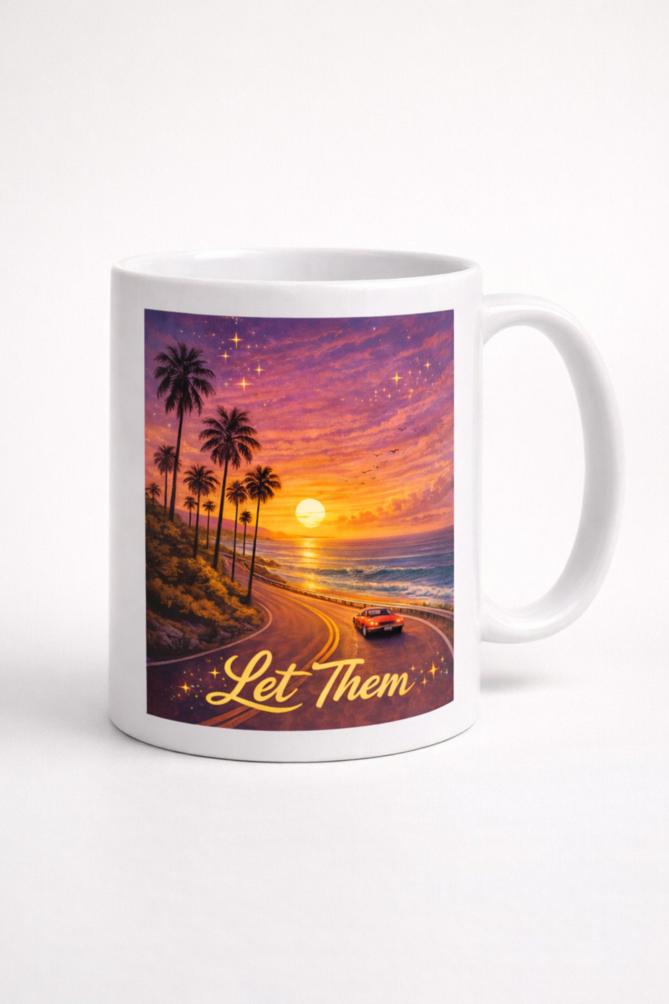 White ceramic mug featuring a sunset coastal road artwork with the words “Let Them”
